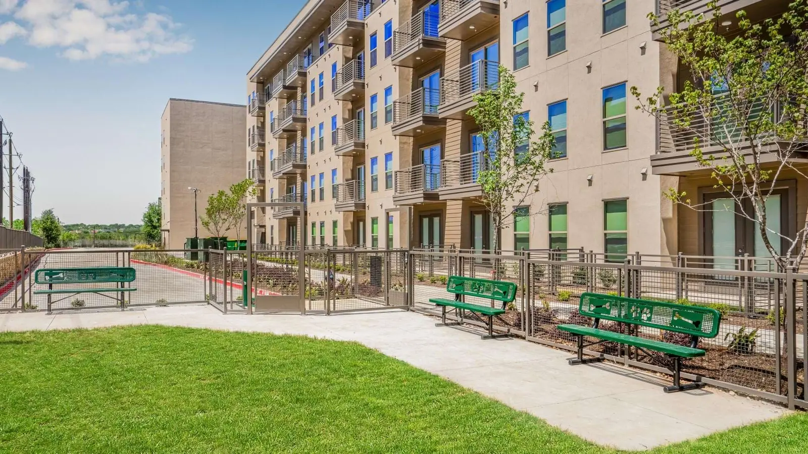 Alta Park Central in Dallas: five-story apartment building with balconies beside a lawn, a paved walkway and green picnic benches