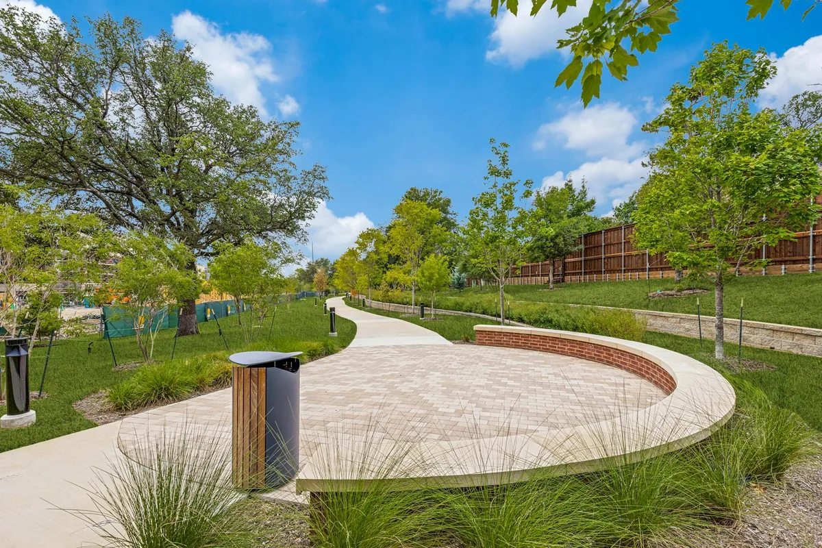 AMLI Treehouse in Addison: curved stone seating wall beside a paved plaza, lawn and young trees on the community grounds