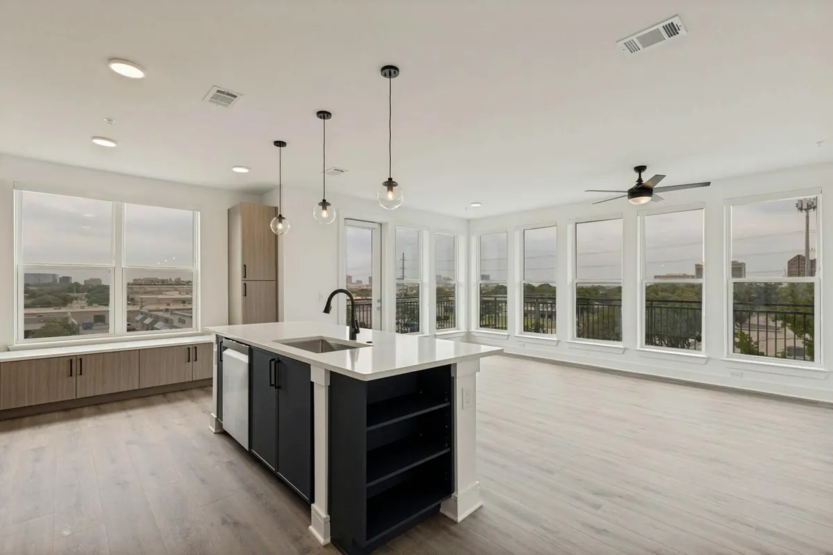 AMLI Treehouse in Addison: open kitchen with a black island, pendant lights and wood-look floors, next to a wall of windows