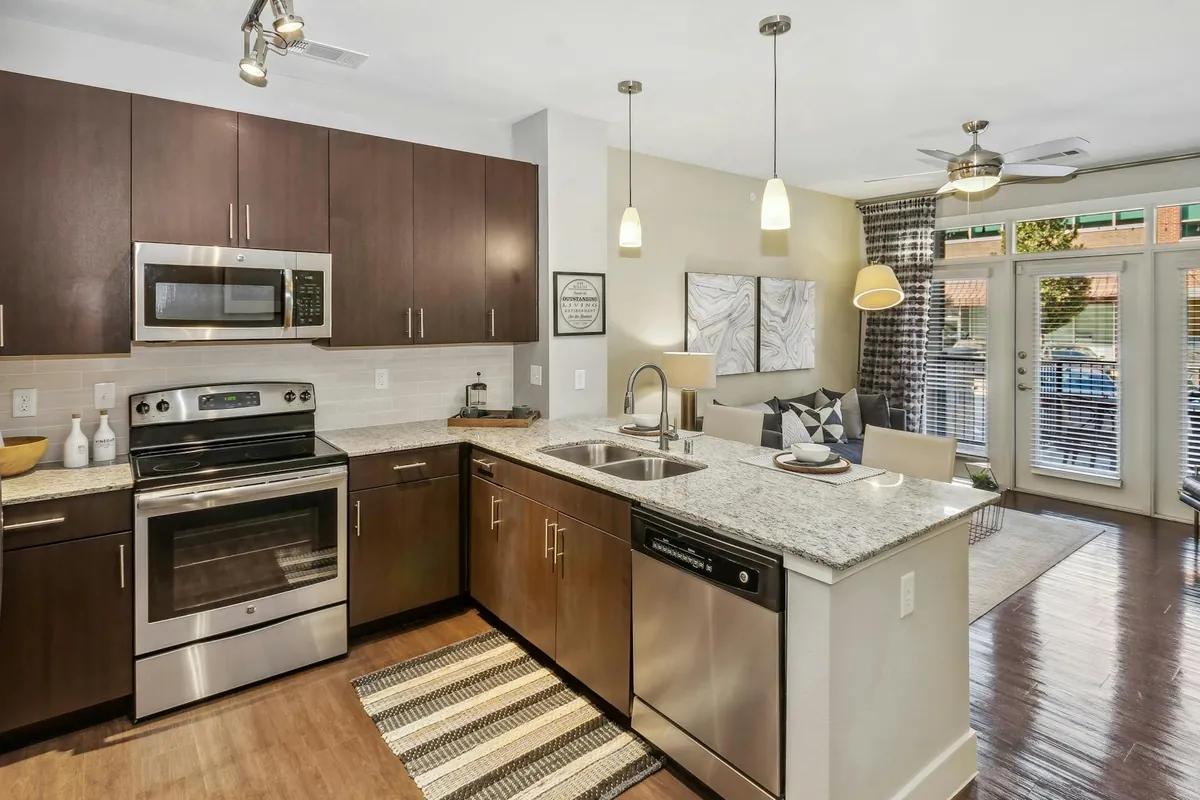AMLI West Plano in Plano: kitchen with dark wood cabinets, granite counters, stainless appliances and pendant lights, open to the living room