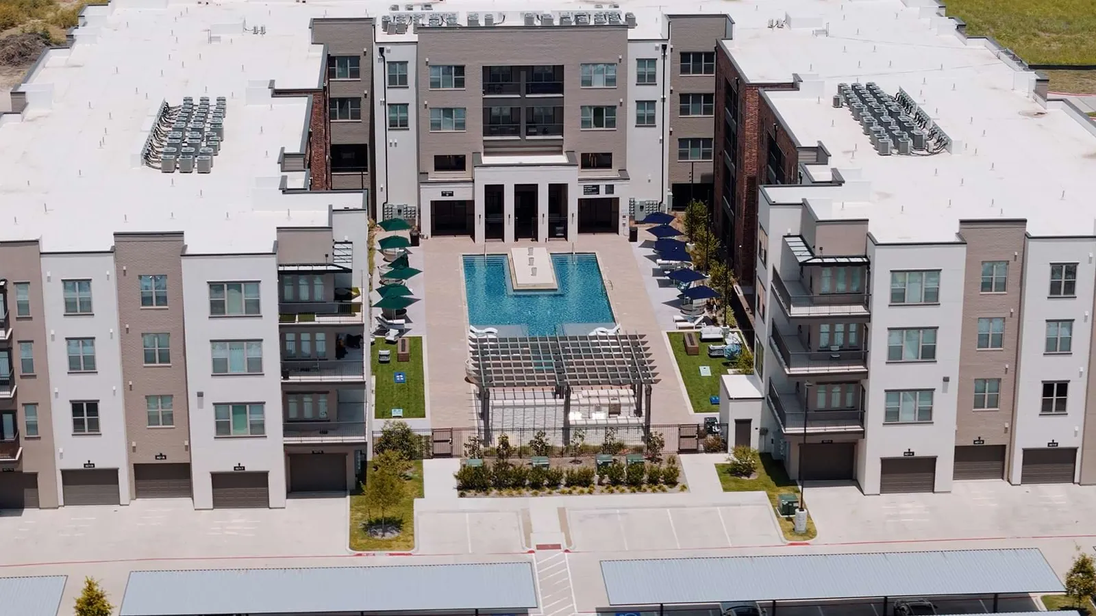 Arden at Midtown GP in Grand Prairie: aerial view of four-story apartment buildings framing a courtyard with a pool and a pergola