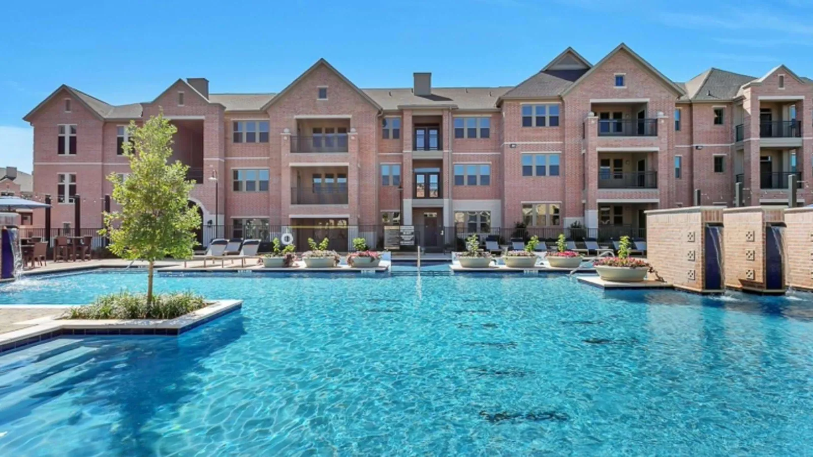Axis Kessler Park in Dallas: three-story brick apartment buildings with balconies behind a large swimming pool under a blue sky