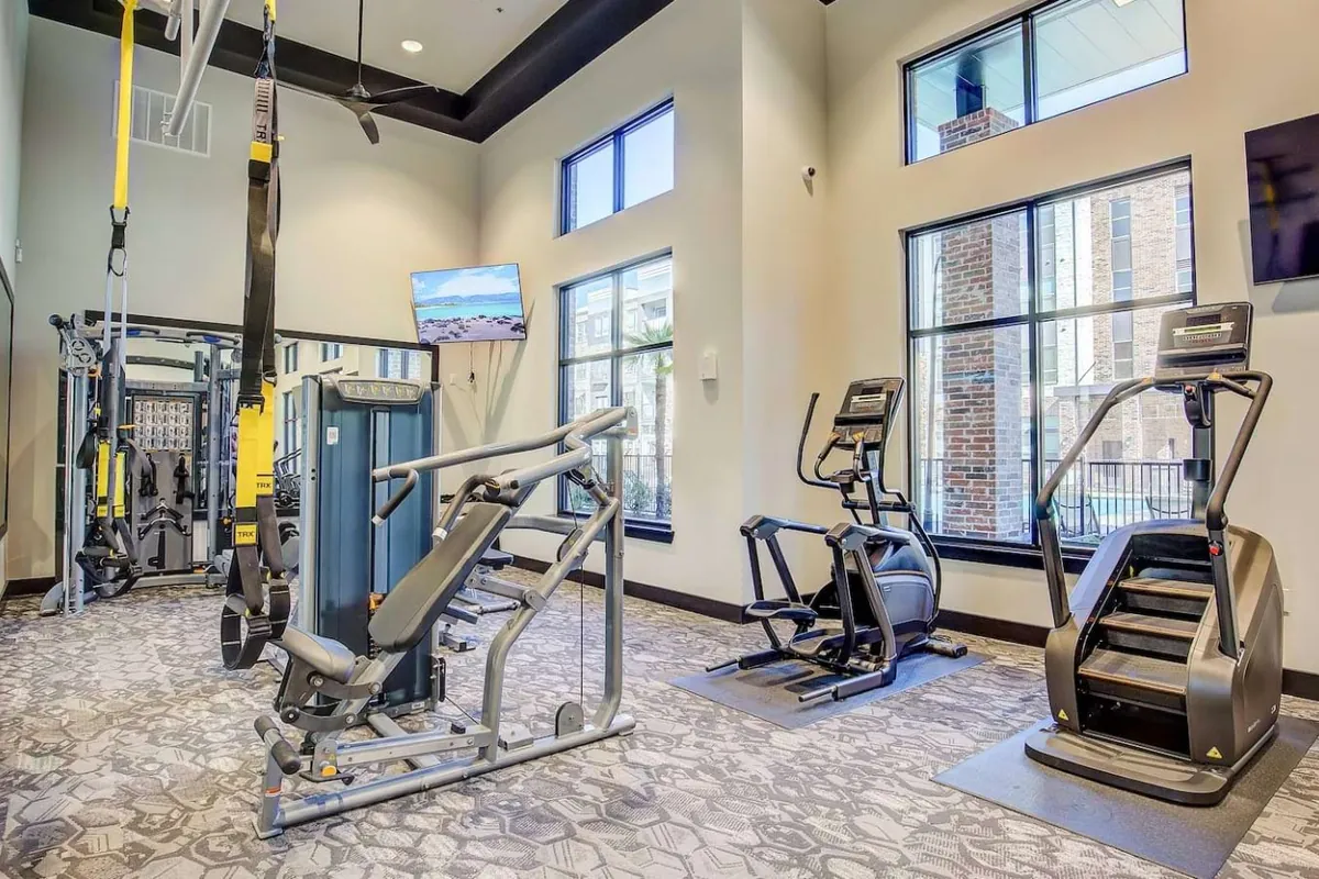 Cole Park in McKinney: fitness center with a functional trainer, elliptical machines and a stair climber beside tall windows
