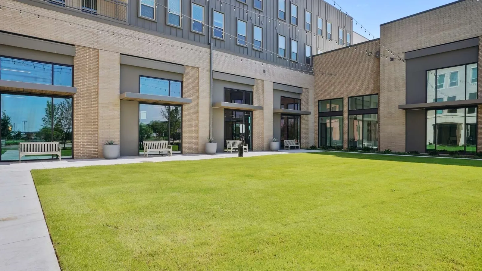 Fairway North Fields in Frisco: courtyard lawn bordered by a four-story tan brick building with large ground-floor windows
