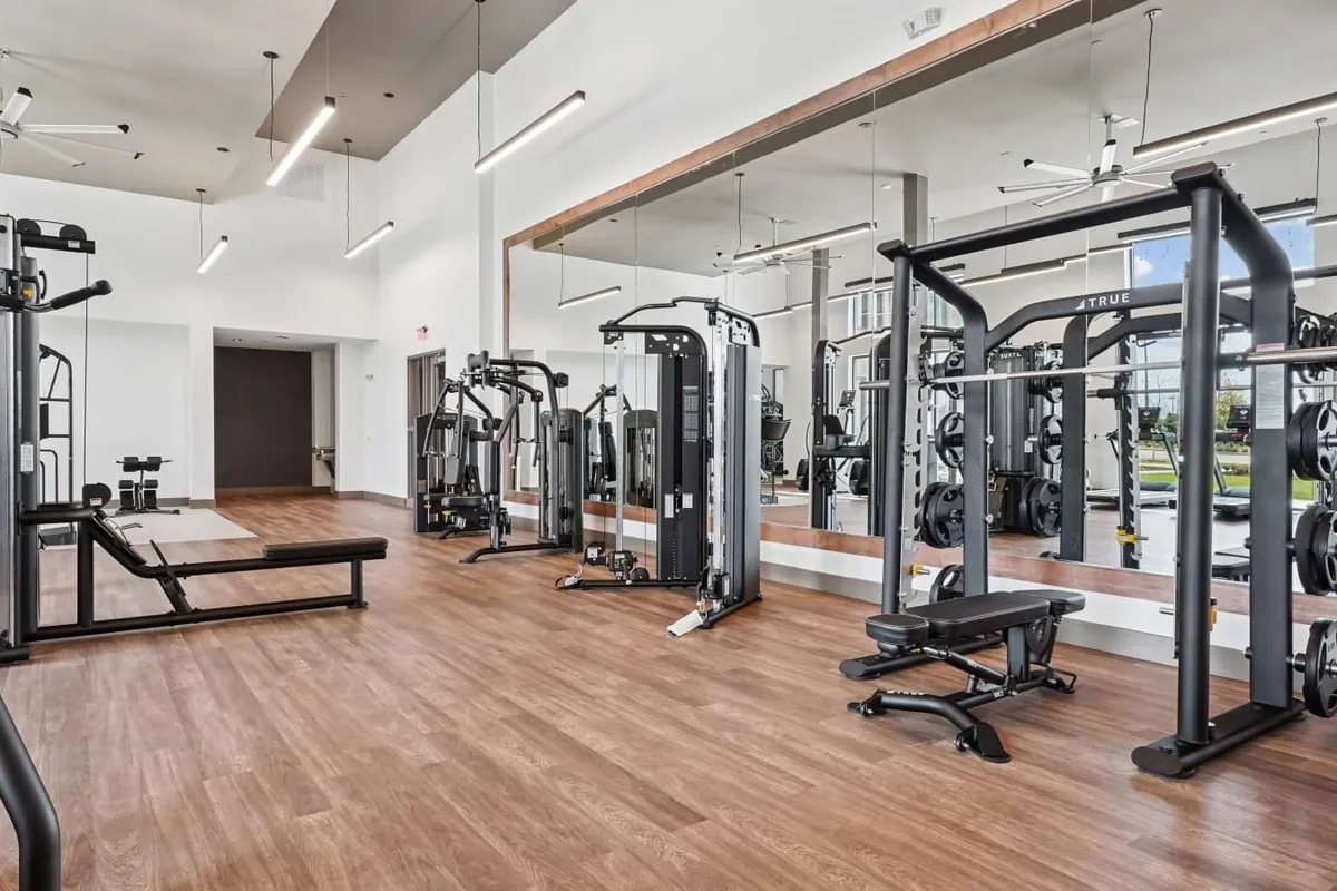 Fairway North Fields in Frisco: fitness center with cable machines and squat racks on wood-look floors, with a mirrored wall