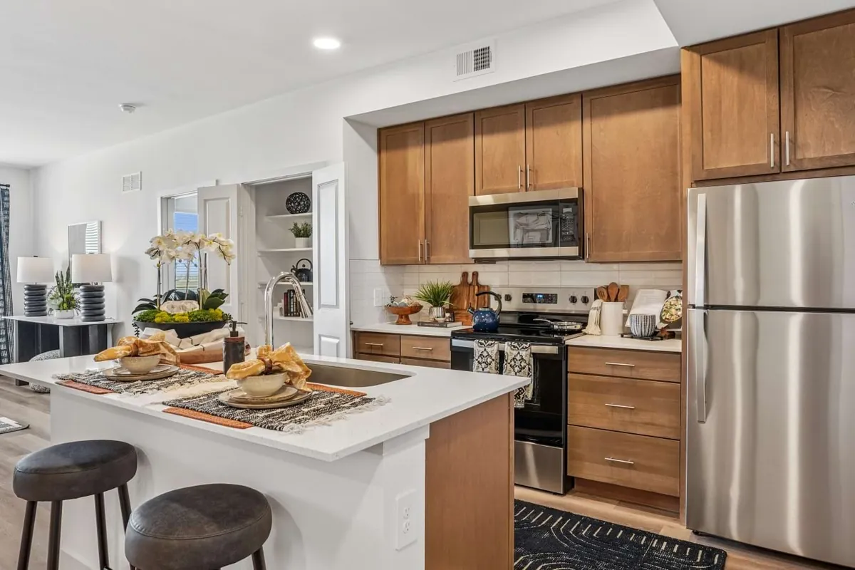 Fairway North Fields in Frisco: kitchen with wood cabinets, a white island with stools and stainless appliances, open to the living area