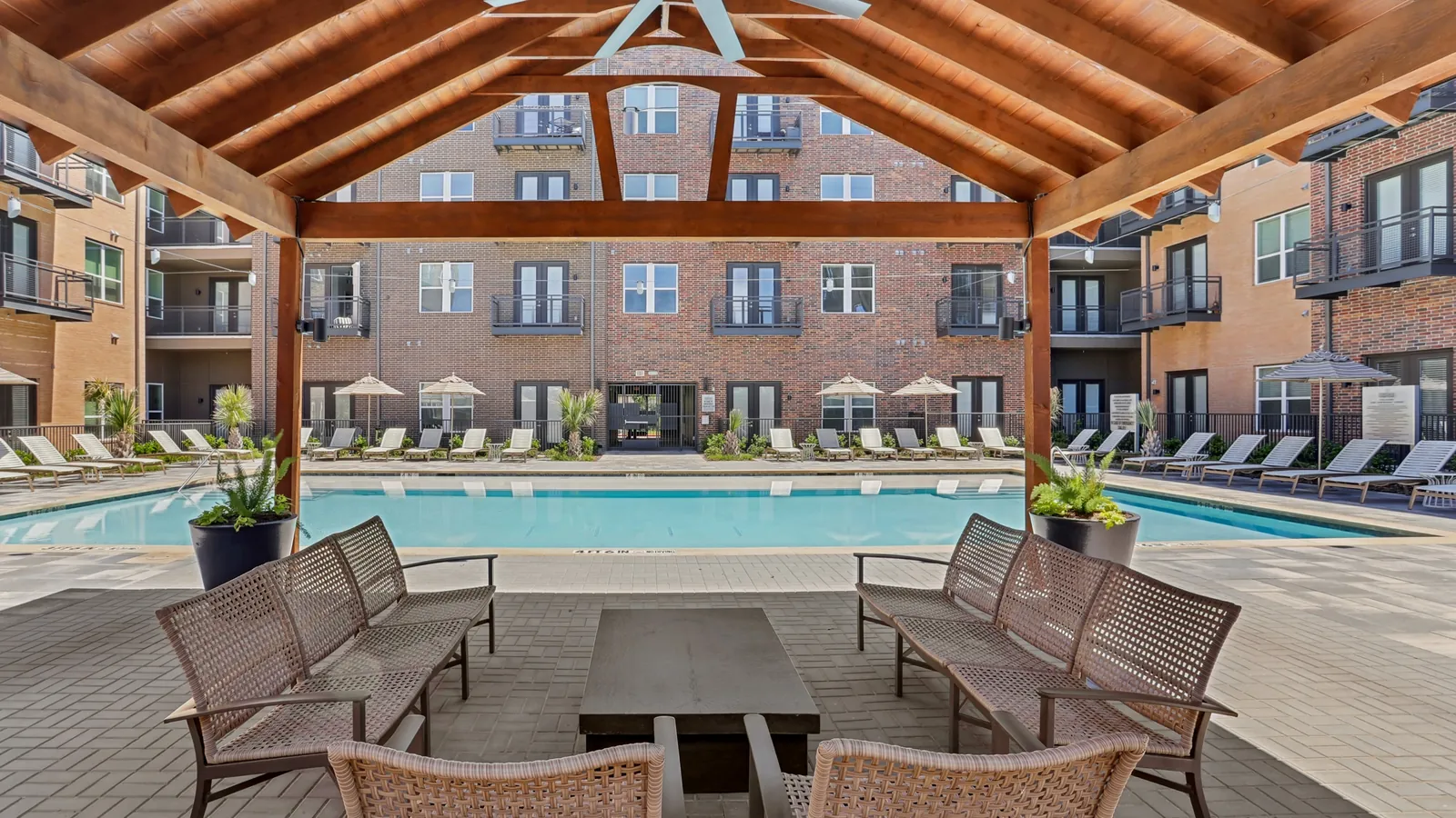 Heritage McKinney Square in McKinney: covered wood pavilion with outdoor seating facing a swimming pool and four-story brick apartment buildings