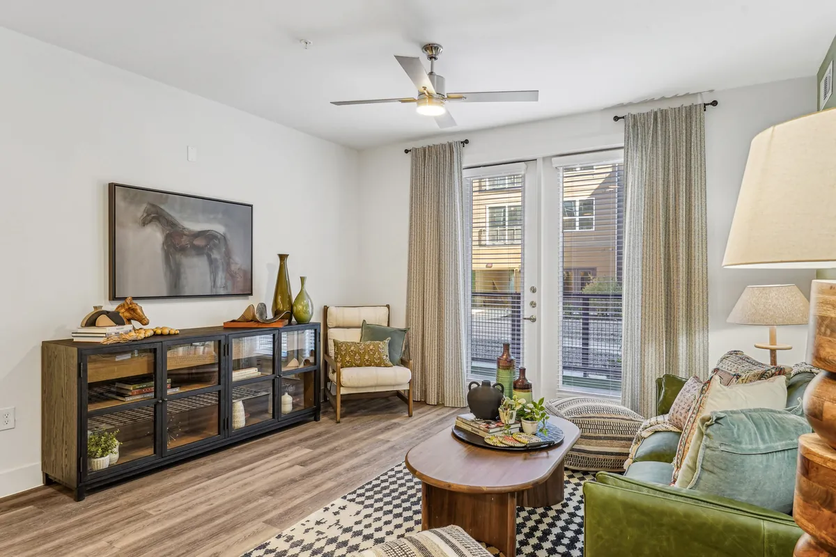 Heritage McKinney Square in McKinney: living room with wood-look floors, a green sofa, a round wood coffee table and glass doors to a balcony