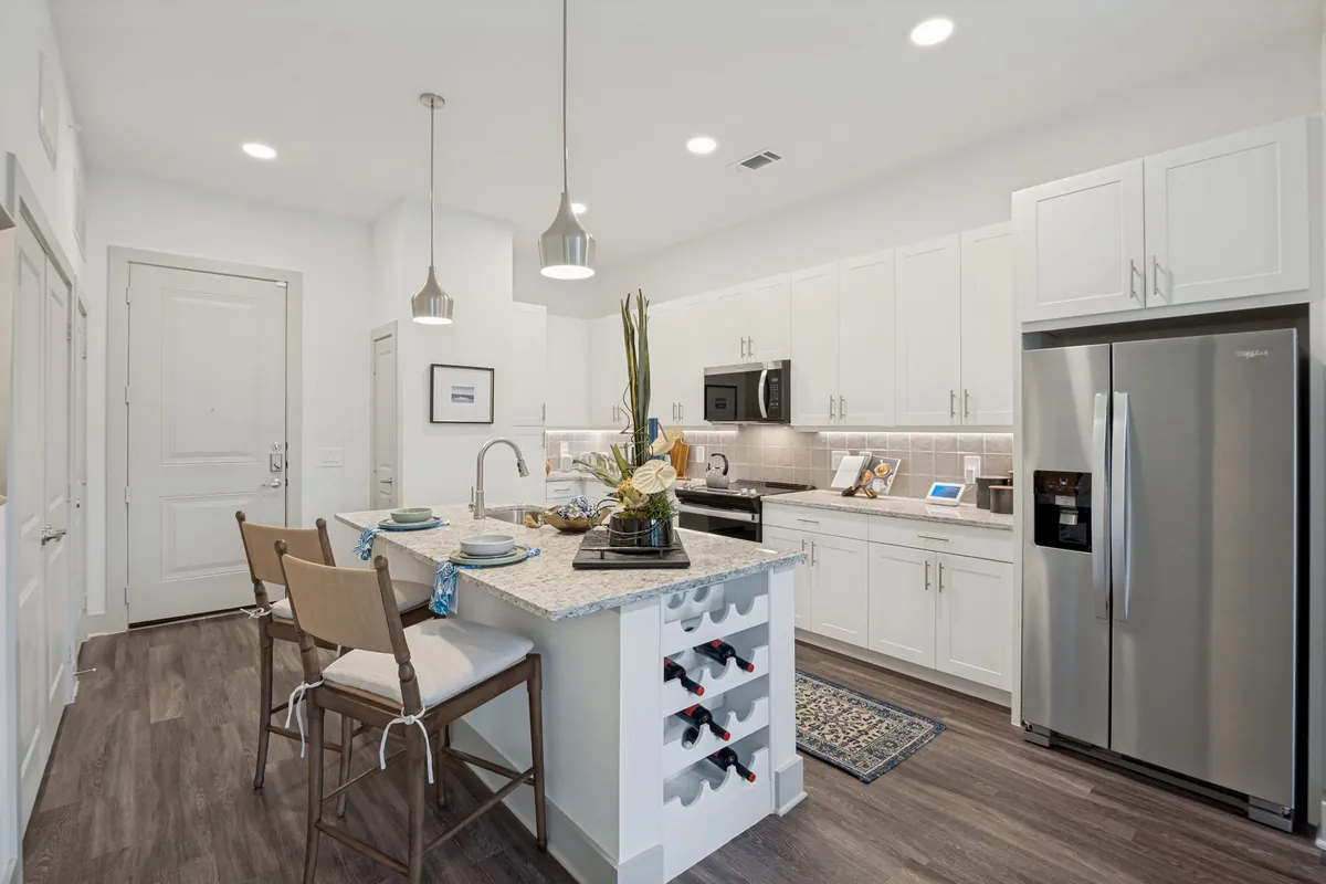 Jefferson Marquee in Lewisville: kitchen with white cabinets, a granite island with a built-in wine rack and stools, and a stainless refrigerator