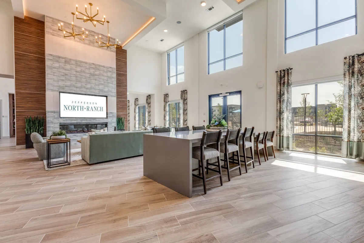 Jefferson North Ranch in McKinney: two-story clubhouse with a stone fireplace wall, a gold chandelier, a sofa and a high-top table with stools