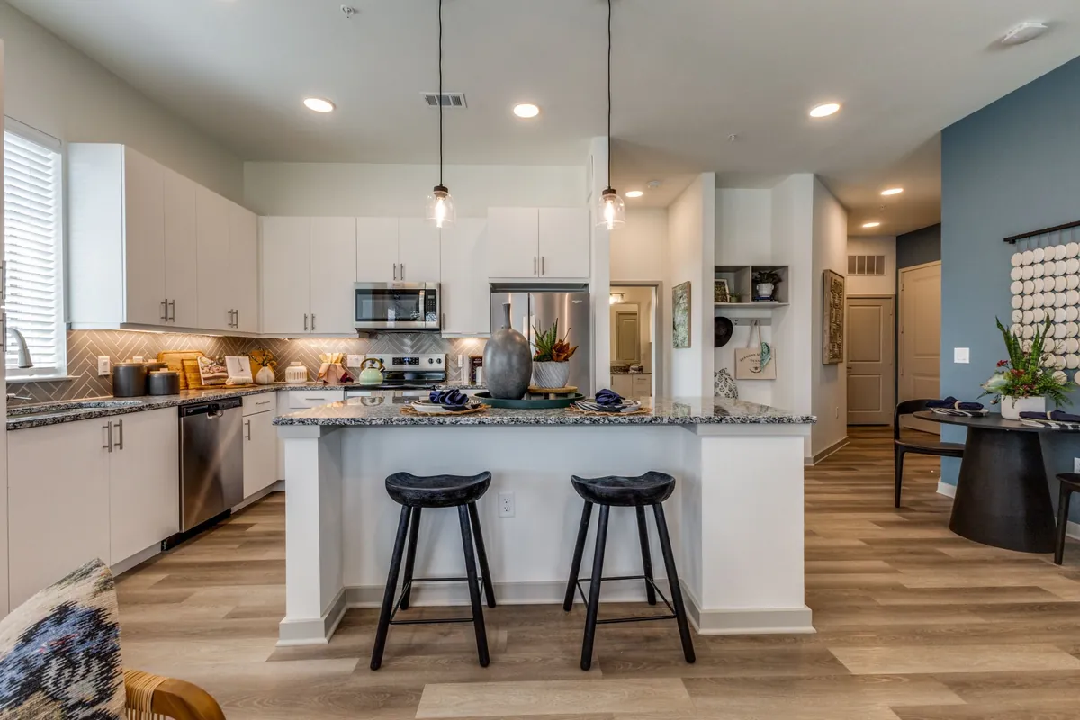 Jefferson North Ranch in McKinney: kitchen with white cabinets, a granite island with two black stools, pendant lights and stainless appliances
