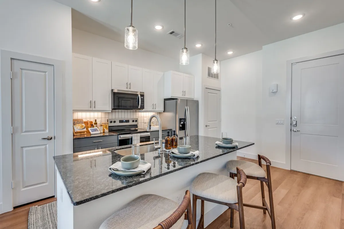 Jefferson Prairie Park in Fort Worth: kitchen with white cabinets, a dark granite island with wood stools, pendant lights and stainless appliances