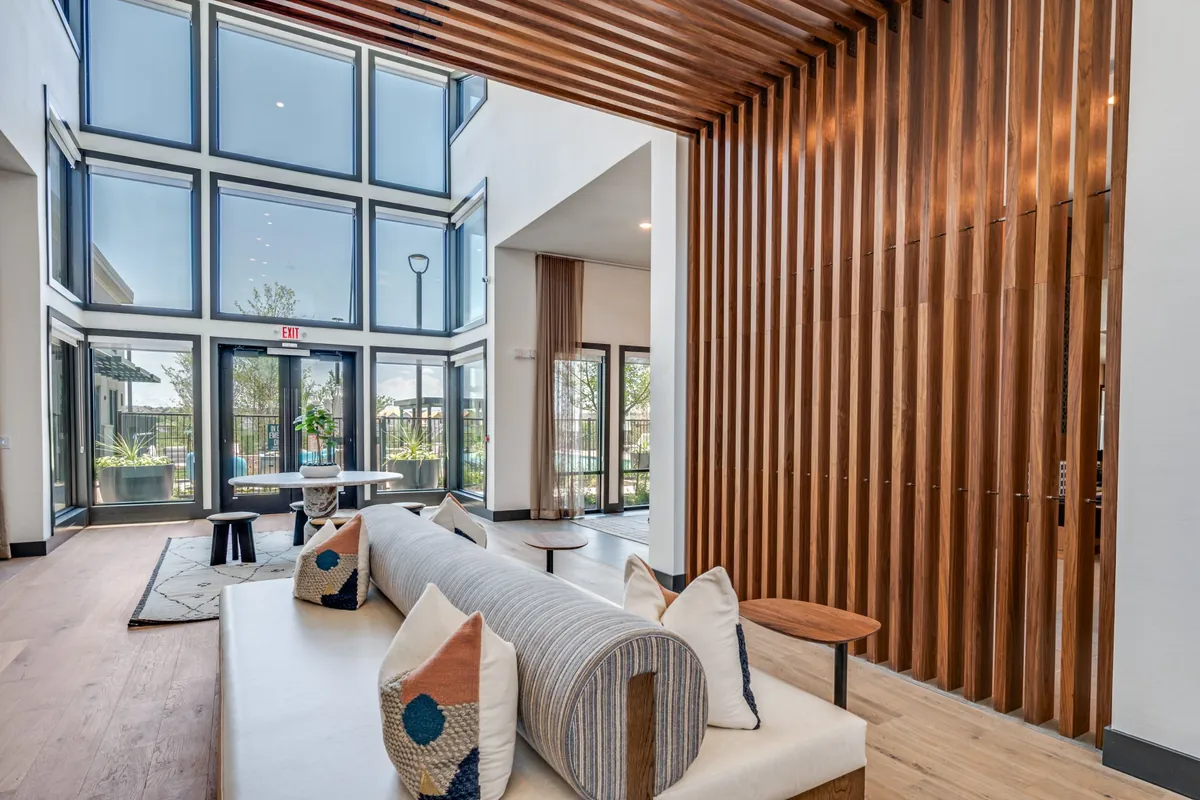 Jefferson Prairie Park in Fort Worth: two-story lounge with a wall of tall windows, a white sofa and a wood slat divider