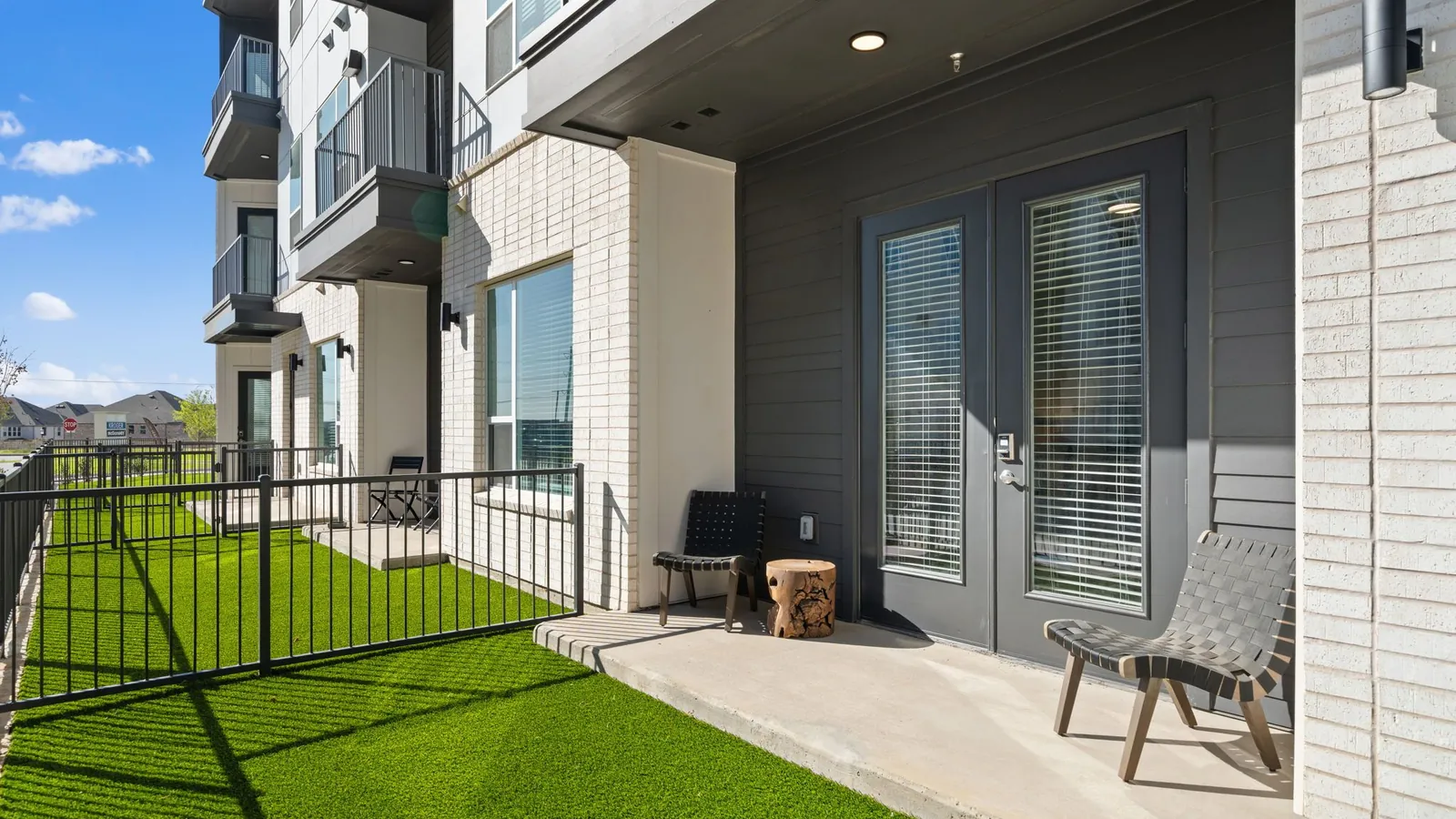Jefferson Union at Castle Hills Marketplace in Lewisville: ground-floor patio with a private artificial-turf yard and a metal fence alongside a four-story apartment building