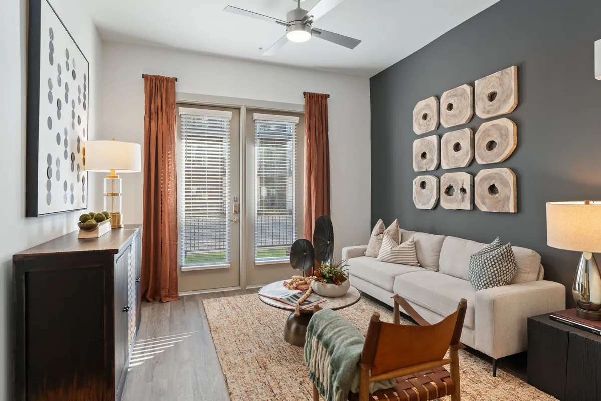 Jefferson Union at Castle Hills Marketplace in Lewisville: living room with a cream sofa, a leather armchair, rust-colored curtains and glass doors to a balcony