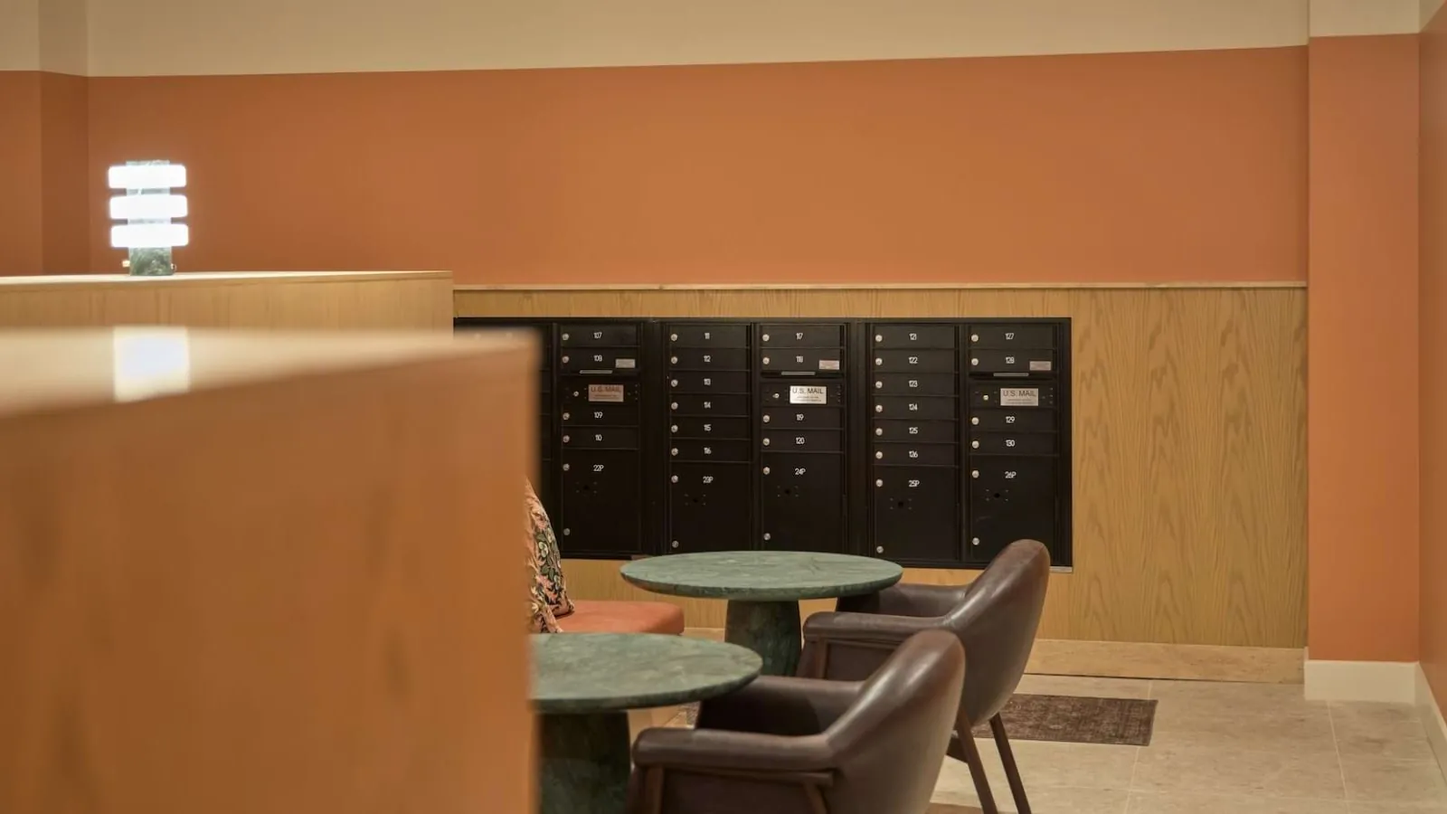 Oakhouse in Dallas: mail room lounge with dark parcel lockers, a round table and leather chairs against terracotta walls