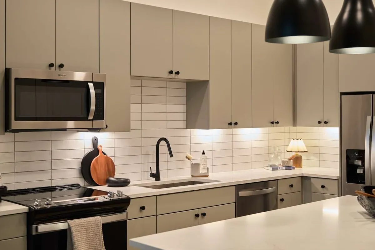 Oakhouse in Dallas: kitchen with gray-green cabinets, white subway tile, black pendant lights and stainless appliances
