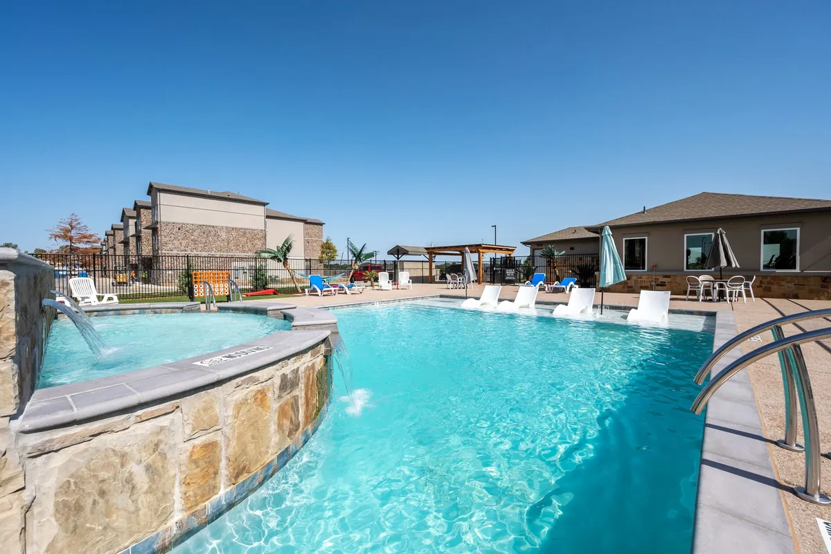 Prairie Gate Community in Grand Prairie: swimming pool with a stone-faced spa and white loungers, with two-story apartment buildings behind under a blue sky