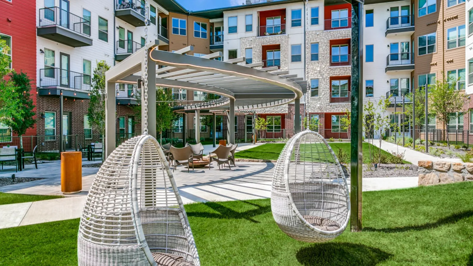 Sagemont in Irving: landscaped courtyard with hanging wicker egg chairs and a shade structure, surrounded by four-story apartment buildings