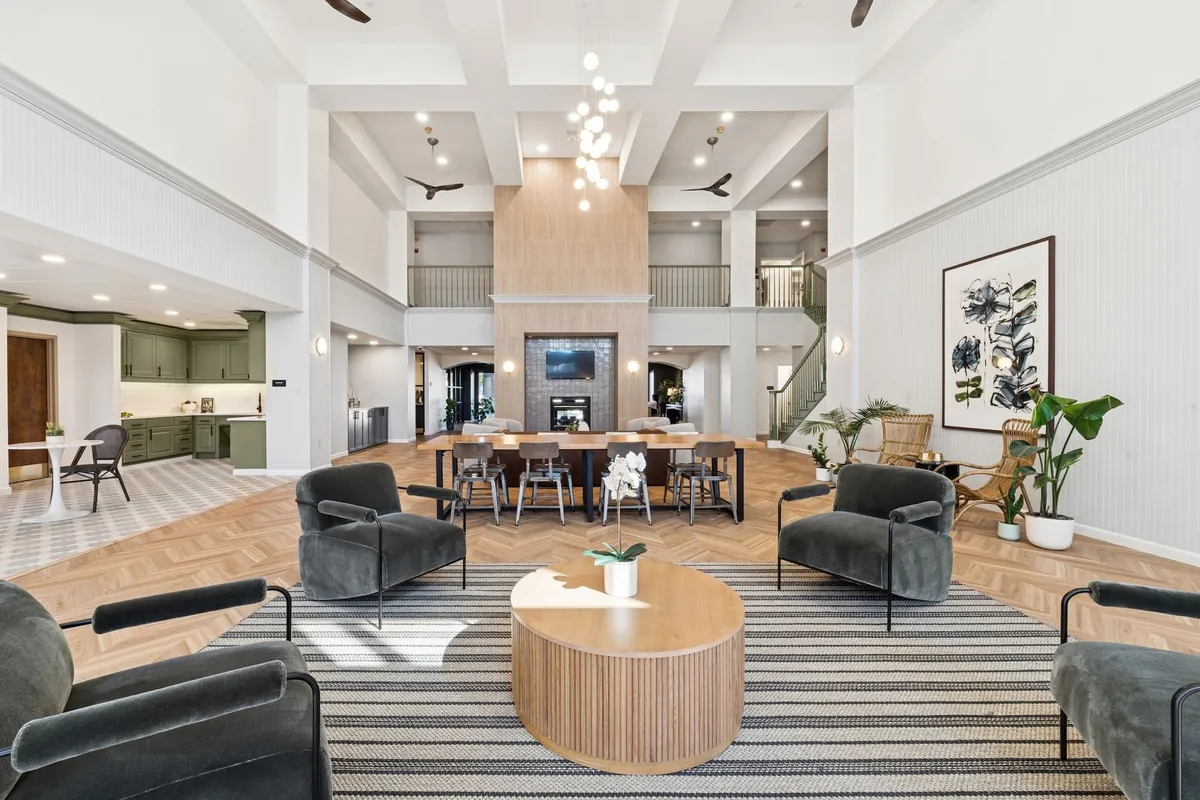 The Ainsley in Dallas: two-story clubhouse lounge with armchairs, a round wood coffee table and a fireplace wall under a beamed ceiling