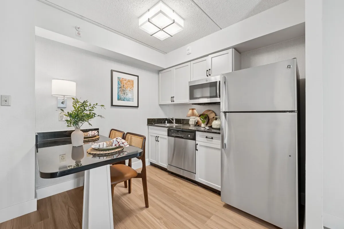 The Ainsley in Dallas: kitchen with white cabinets, a stainless refrigerator and dishwasher, and a small dining table with two chairs