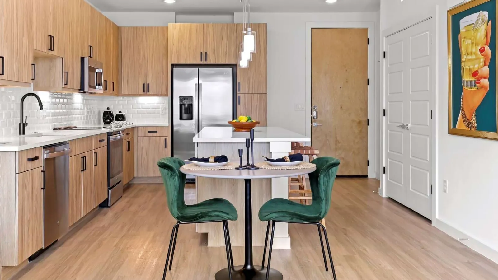 The Boheme in Dallas: kitchen with light wood cabinets and a white island, with a small round table and green chairs in front