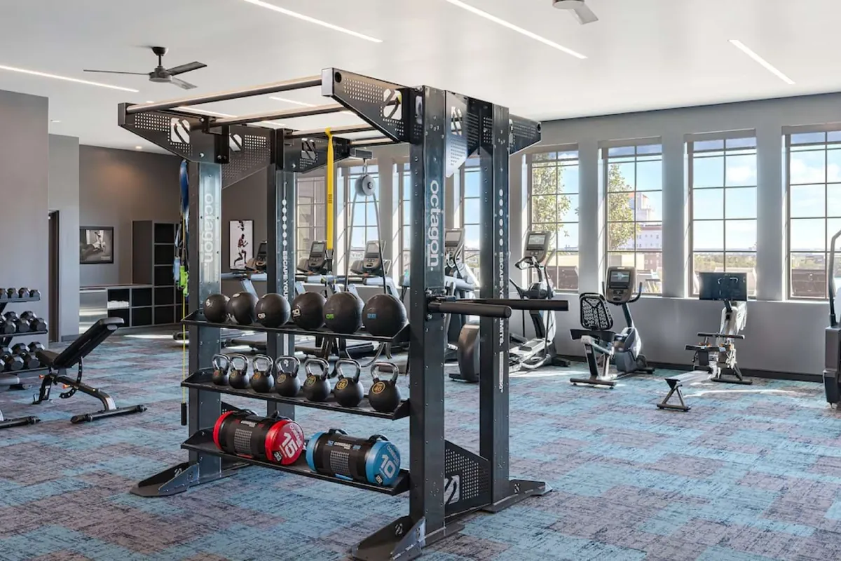 The Boheme in Dallas: fitness center with a squat rack, dumbbells and cardio machines next to tall windows