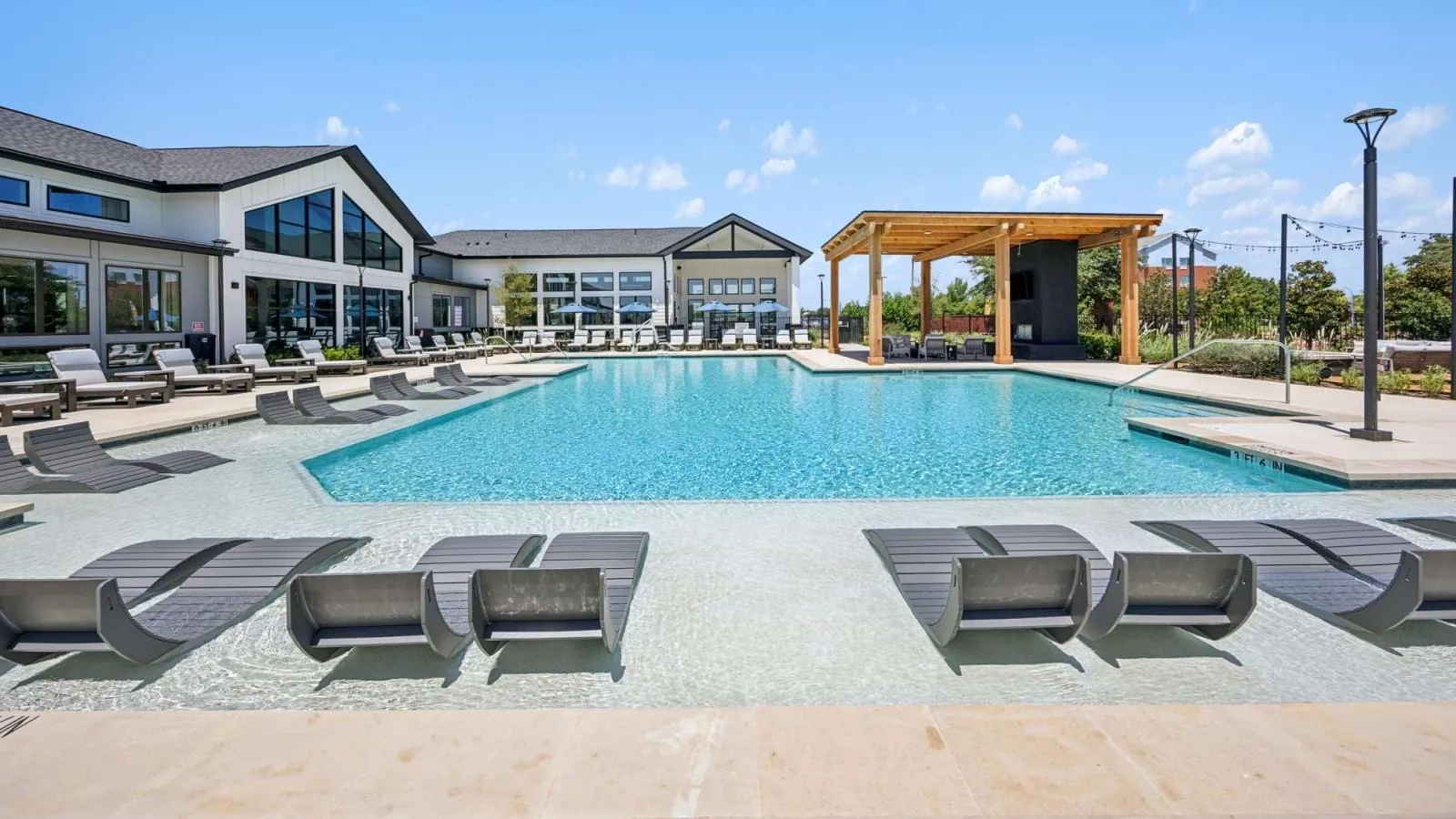 The Dalton in McKinney: large swimming pool with in-water loungers and a pergola in front of a dark-roofed clubhouse building