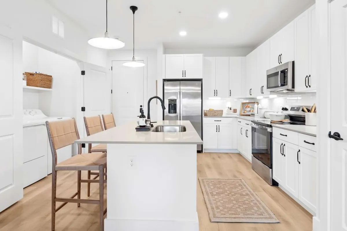 The Dalton in McKinney: kitchen with white cabinets, a white island with wicker stools, pendant lights and a stainless refrigerator