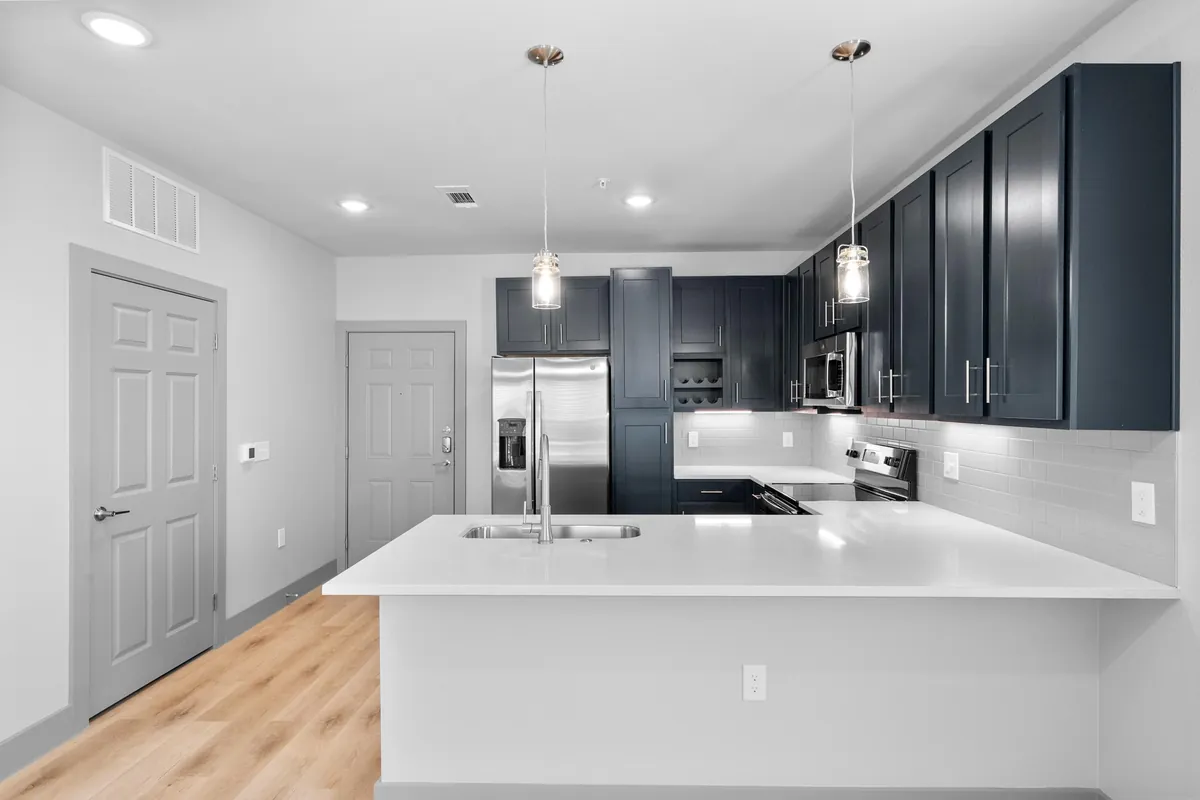 The Gibson in Grand Prairie: kitchen with navy cabinets, a white peninsula, pendant lights and stainless appliances on light wood-look floors