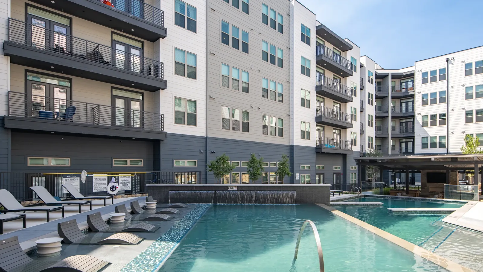 The Huntley in Fort Worth: five-story apartment buildings with balconies wrapped around a pool courtyard with loungers, under a blue sky