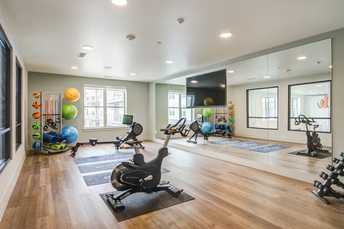 The Huntley in Fort Worth: fitness studio with wood-look floors, exercise bikes, a rowing machine, a rack of exercise balls and a wall mirror