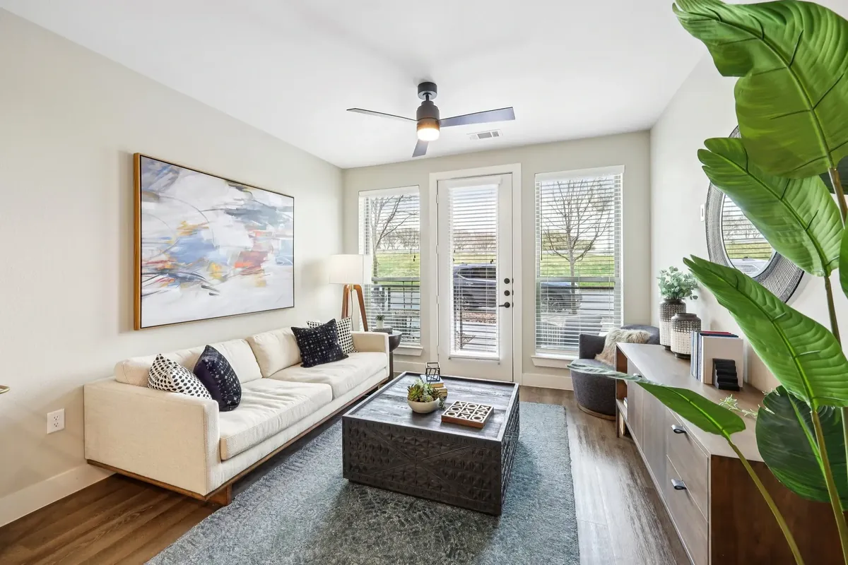 The Huntley in Fort Worth: living room with a white sofa, a dark coffee table, a large plant and glass doors to a patio