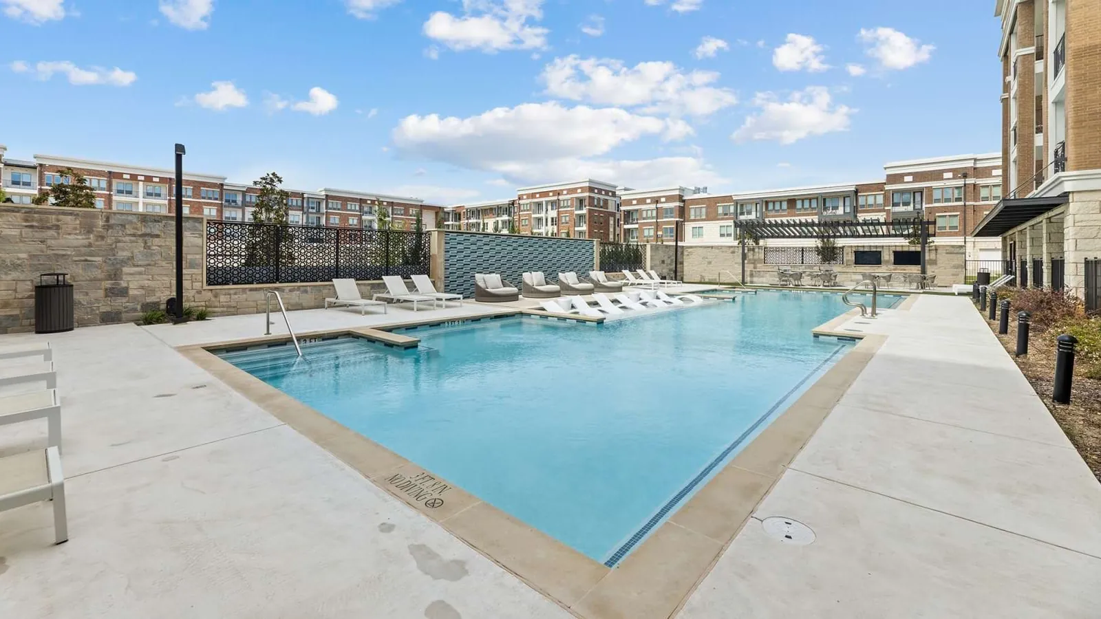 The Links On PGA Parkway in Frisco: swimming pool with white loungers surrounded by four-story brick apartment buildings under a partly cloudy sky