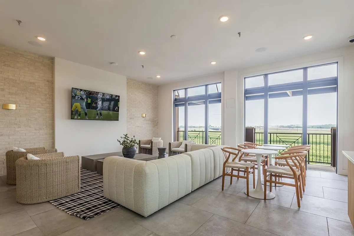 The Links On PGA Parkway in Frisco: clubhouse lounge with a white sofa, armchairs and a dining table beside floor-to-ceiling windows