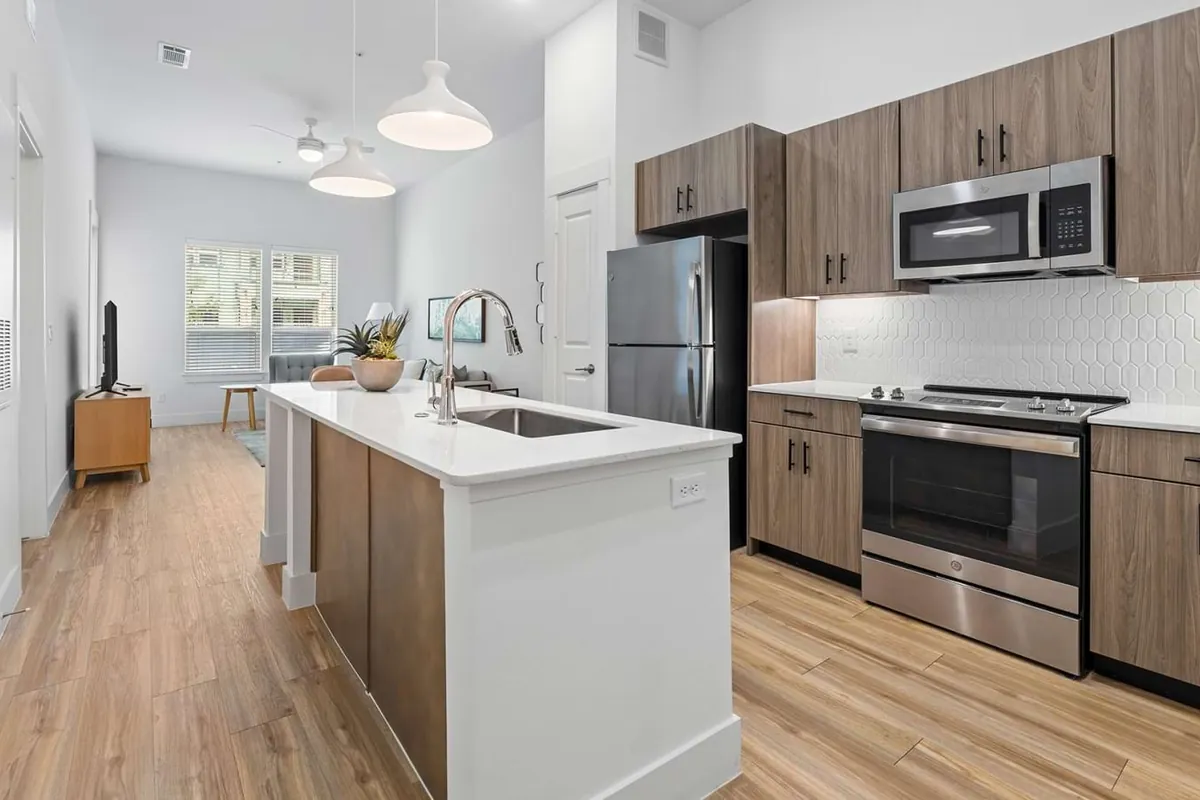 The Links On PGA Parkway in Frisco: galley kitchen with wood-grain cabinets, a white island with a sink, stainless appliances and light wood-look floors