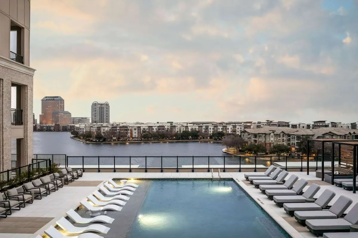 The Mustang in Irving: pool deck with rows of white loungers overlooking a lake and mid-rise buildings at sunset