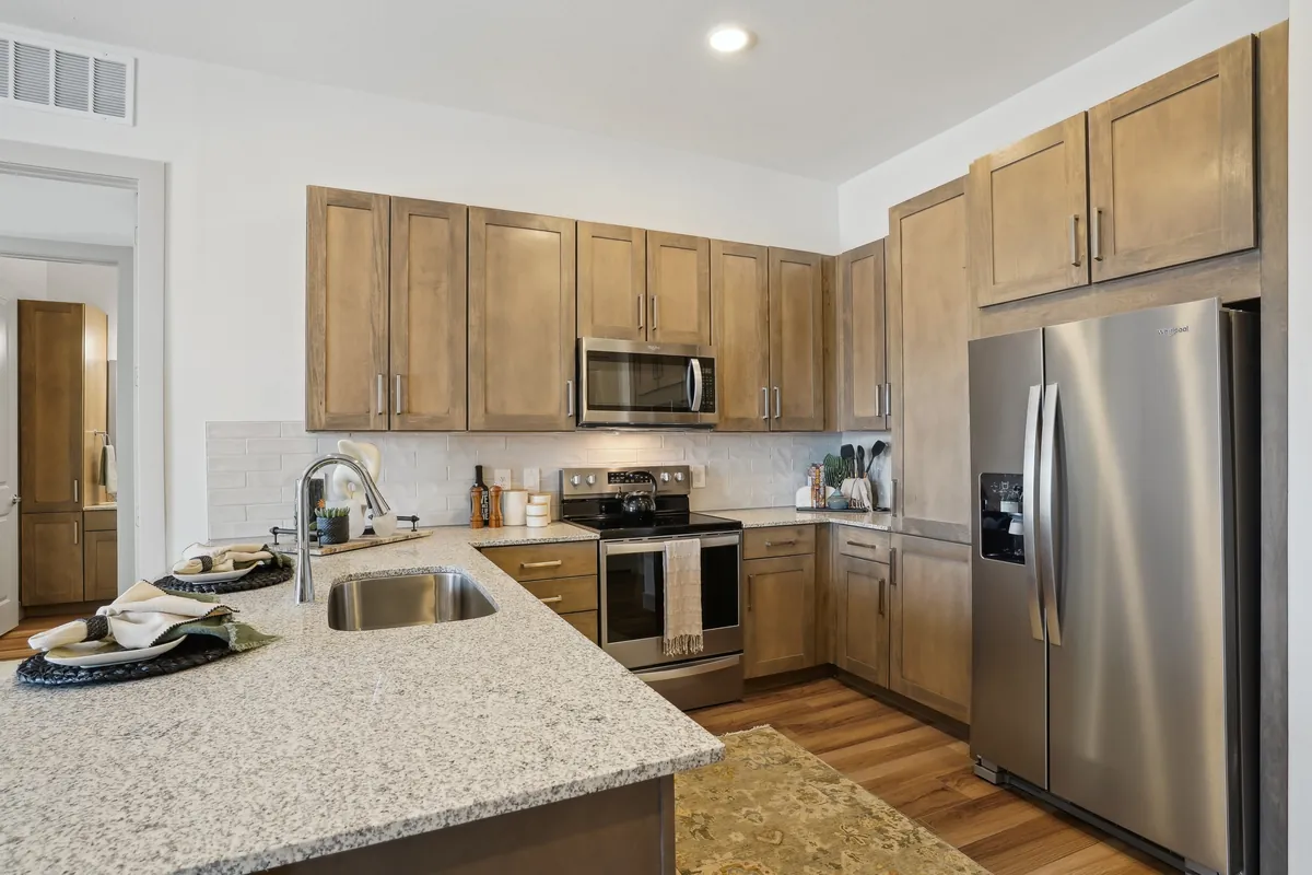 The Residences at Promontory in Plano: kitchen with wood cabinets, a granite peninsula with a sink and stainless appliances