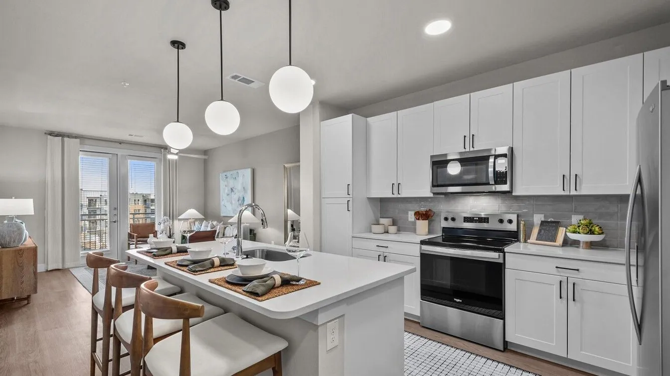 The Storey in Dallas: kitchen with white cabinets, a white island with wood stools, three globe pendant lights and stainless appliances
